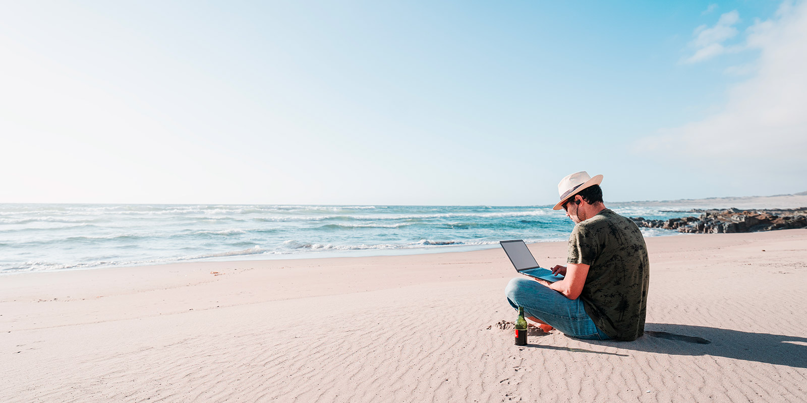 man sitting beach drinking beer with laptop alone